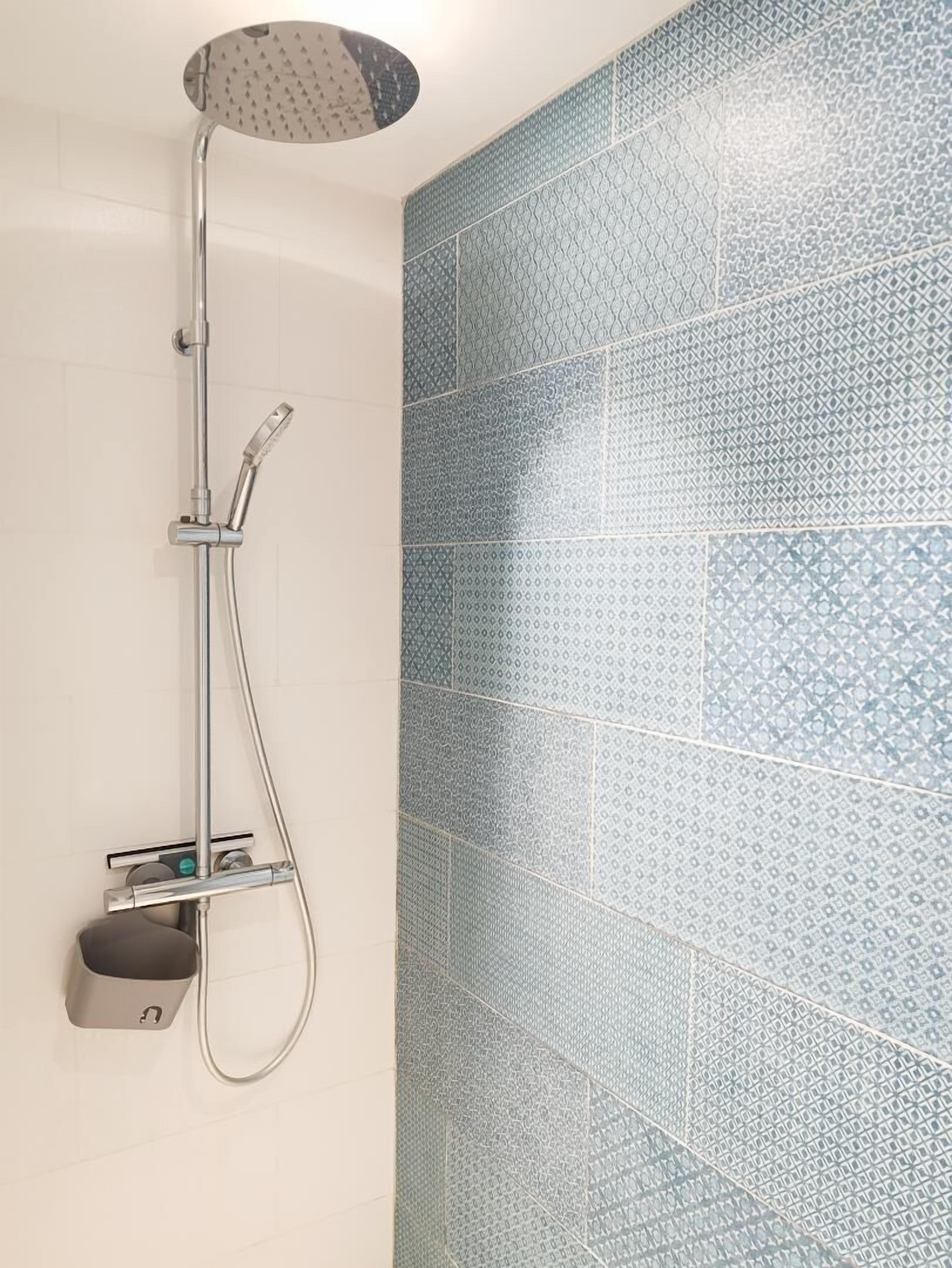 A shower with a rain showerhead and handheld showerhead, a handheld soap dispenser, and a towel rack.