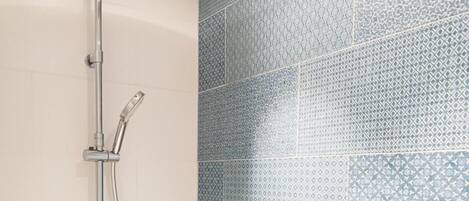 A shower with a rain showerhead and handheld showerhead, a handheld soap dispenser, and a towel rack.