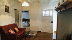 Ein Wohnzimmer mit einem roten Sofa, einem Glastisch, Holzböden und einer weißen Tür mit schmiedeeisernen Verzierungen.