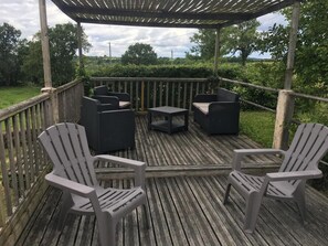 Une terrasse en bois, agrémentée de mobilier d’extérieur, notamment des chaises et une table, et entourée d’une balustrade en bois.