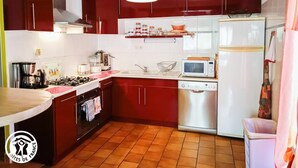 Une cuisine de taille réduite avec des meubles rouges, un réfrigérateur en acier inoxydable, un four à micro-ondes et une cuisinière à gaz.