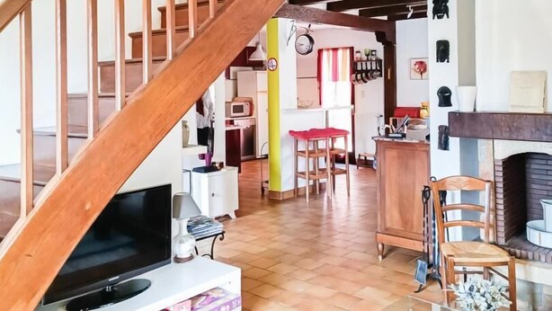 Un vaste espace de vie agrémenté d’un escalier en bois menant à l’étage supérieur, d’une télévision et d’une cheminée.