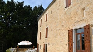 Ein Steinhaus mit Terrasse, Sitzgelegenheiten im Freien und einem großen Sonnenschirm.