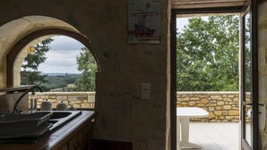 Eine rustikale Küche mit einer Steinwand, einem Spülbecken und einem Fenster mit Blick auf eine Steinterrasse und eine grüne Hügellandschaft.