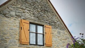 A stone house with a wooden exterior, a large sliding glass door, and a wooden picnic table in the foreground. - Gîtes de France® - My Loft (ST CIRQ SOUILLAGUET)