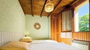 Un dormitorio con una cama, una lámpara de noche, un adorno circular en la pared, contraventanas de madera y una ventana con vistas a la vegetación.