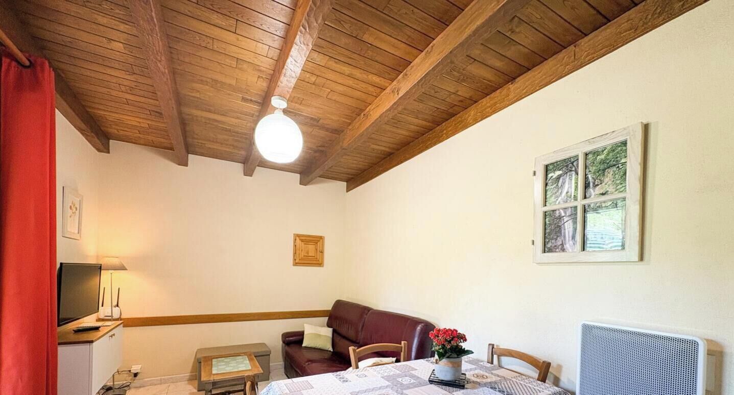 Ein Zimmer mit Holzboden, einem Tisch mit Blumenvase, einer Couch, einem gerahmten Bild an der Wand und einem Fenster.