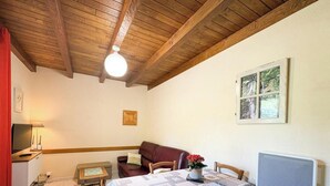 Una habitación con techo de madera, una mesa con un florero, un sofá, un cuadro en la pared y una ventana.