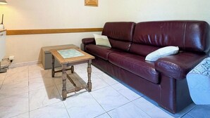 Una sala de estar con un sofá de cuero marrón, una mesa de centro de madera y piso de baldosas.