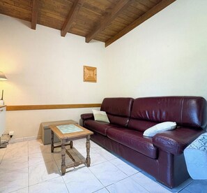 A living room with a brown leather sofa, a wooden coffee table, and a tiled floor.