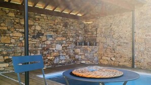 Et udendørs område med stenvægge, en pool, et rundt bord med en vævet dug og en blå stol.
