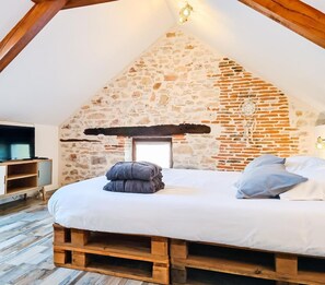 Un dormitorio con pared de piedra, estructura de cama de madera, televisor sobre un mueble de madera y un atrapasueños en la pared.