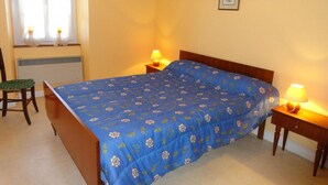 Quarto com cama, duas mesas de cabeceira com luminárias, uma cadeira e uma janela com cortinas.