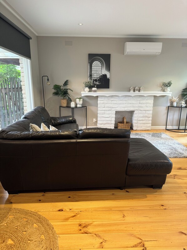 A modern living room with a black leather sofa, a white fireplace, and a large window.