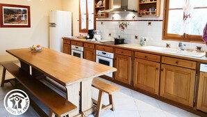 Une cuisine avec des meubles de rangement en bois, une cuisinière, un évier et une table à manger avec des bancs.