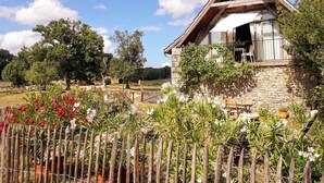 A stone house with a wooden balcony, surrounded by a garden with various plants and flowers. - Gîtes de France® - The Demolished Barn (ASSIER)