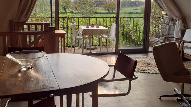 A cozy room with a large table and chairs, a balcony with a view of greenery, and a rustic interior design. - Gîtes de France® - The Demolished Barn (ASSIER)