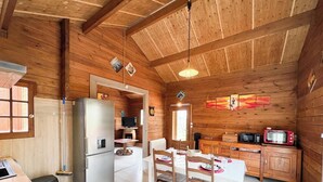 Interior de una cabaña de madera con una mesa de comedor, sillas, un refrigerador, un microondas y un televisor.