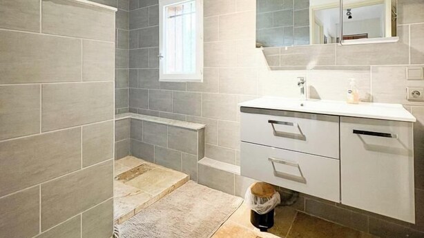 A bathroom with grey tiles, a window, a mirror, a sink, and a shower area. - Gîtes de France® - My Little Paradise (CARNAC ROUFFIAC)