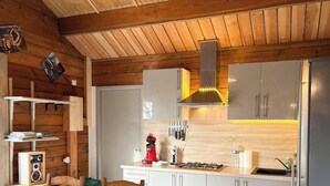 Una cocina moderna con paredes de madera, una estufa a gas, una cafetera roja y un refrigerador de acero inoxidable.