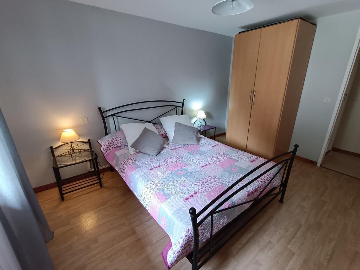 A bedroom with a bed, a wardrobe, a nightstand with a lamp, and a wooden floor.
