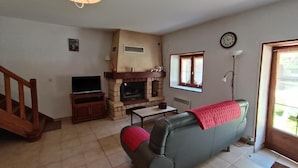 A living room with a fireplace, sofa, television, and a staircase. - Gîtes de France® - La Grange (SAINT-MARTIN-LABOUVAL)