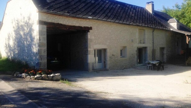 A two-story building with a large garage door, a small attached structure, and a gravel driveway.