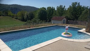 Una piscina rectangular de agua cristalina y azul, rodeada por un muro de piedra y una solana pavimentada.