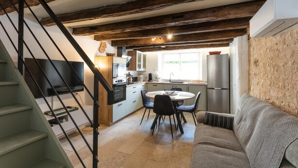 A modern kitchen with a dining area, a staircase, and a living room with a sofa.