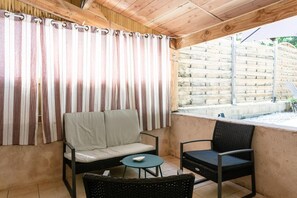 Un patio techado con un sofá acolchado, una mesita redonda y una silla de mimbre.