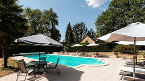 A swimming pool with lounge chairs and umbrellas, surrounded by trees and a stone building.