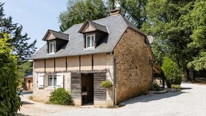 A stone house with a sloped roof, a chimney, and a small porch with a hanging planter.