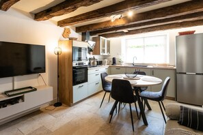 A modern kitchen with a TV, oven, and dining area with chairs and a table.