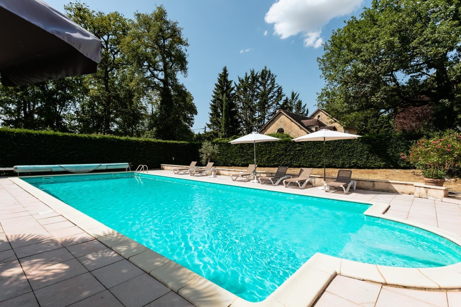 A swimming pool with lounge chairs and umbrellas, surrounded by trees and a building.
