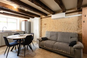 A cozy room with a stone wall, a wooden ceiling, a grey sofa, and a dining table with chairs.