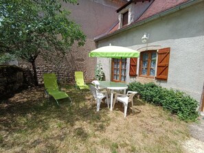 outdoor seating area with a round table and four chairs, surrounded by a low stone wall and a hedge.