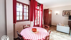 Un comedor con una mesa redonda cubierta por un mantel a cuadros rojo y blanco, sillas de madera y un armario de madera.