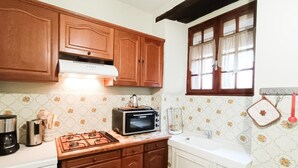 Una cocina con armarios de madera, estufa a gas, microondas y una ventana con cortinas.