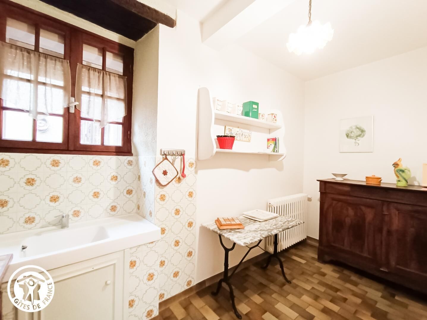Cucina con piano di lavoro bianco, mobiletto in legno, termosifone e ripiano con oggetti da cucina.