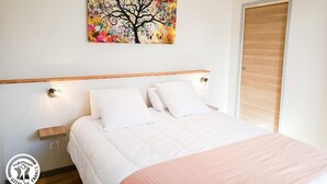 Een slaapkamer met een bed, nachtkastje, houten hoofdbord, een kunstwerk aan de muur en een houten deur.