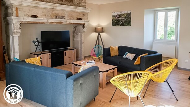 Een woonkamer met een open haard, een televisie, een bank en twee gele stoelen.