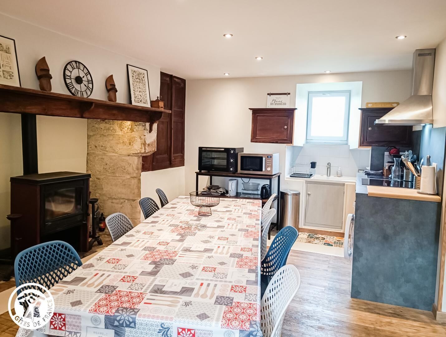 A cozy kitchen with a long dining table, wooden cabinets, and a stone wall.
