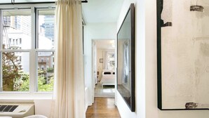 A hallway with a wooden floor, a bed, and a large window with curtains. - The Diplomat #3 - Boutique Designer Home (New York)