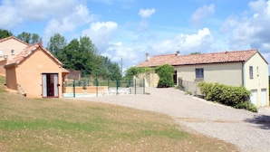 Una zona residencial con dos casas, una con techo de tejas rojas y otra con fachada color beige. Se observa un área de piscina cercada con una silla y una mesa.