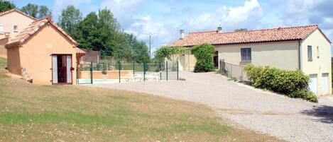 A residential area with two houses, one with a red-tiled roof and another with a beige exterior. There is a fenced pool area with a chair and a table.