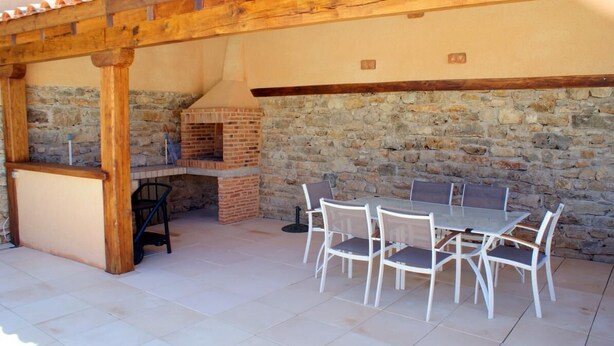 Un patio exterior con muro de piedra, horno de ladrillo y una mesa con sillas.