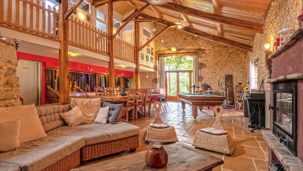 Un interior acogedor y rústico con techo de madera, paredes de piedra, una mesa de billar y chimenea.