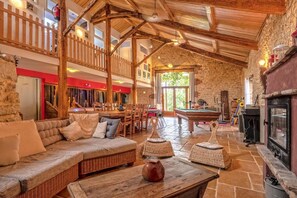A cozy, rustic interior with a wooden ceiling, stone walls, a billiards table, and a fireplace. - Gîtes de France® - La Grange de Janes (MAUROUX)
