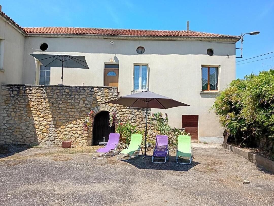 Un edificio con muro de piedra, un patio cubierto con sillones de descanso y techo de tejas.