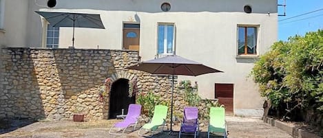 A building with a stone wall, a covered patio with lounge chairs, and a tiled roof.